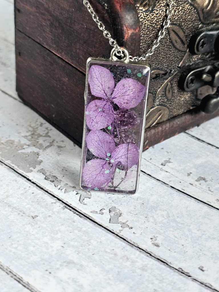 small purple flowers in clear resin held in a silver rectangular bezel frame
