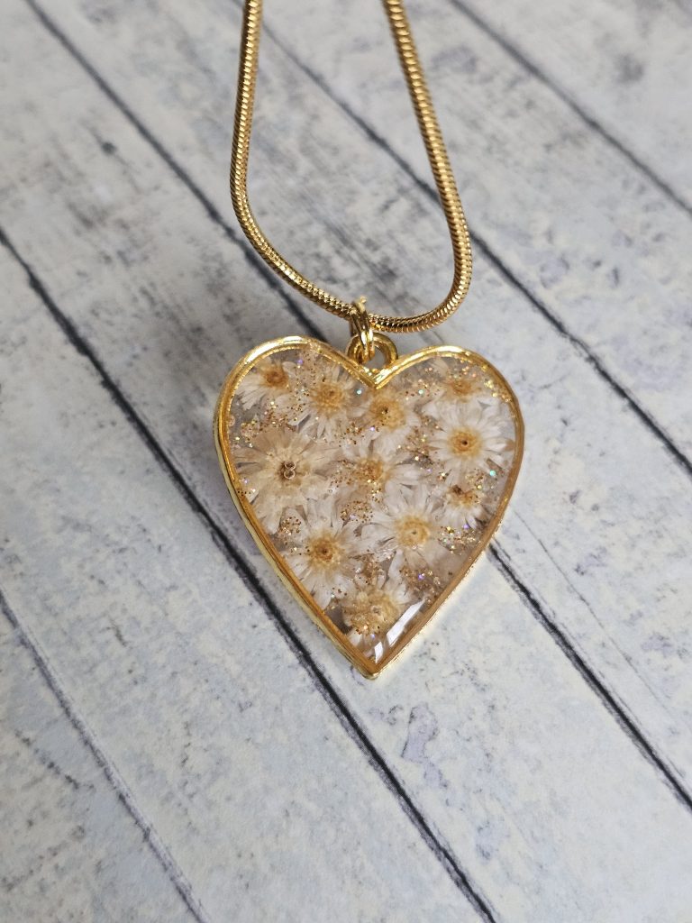 Daisies in an gold tone gold bezel on a gold tone chain on a white wooden background.