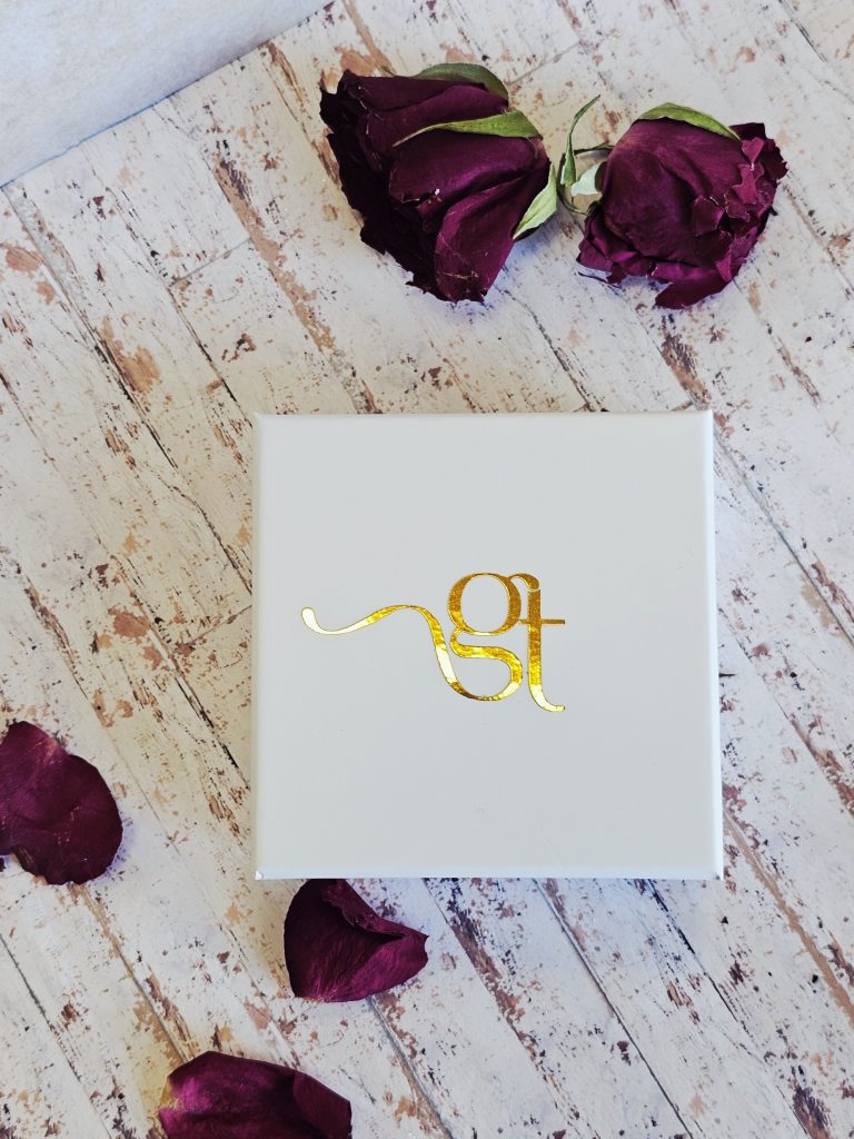White Gifts And Thoughts Gold Embossed Gift Box on a white wooden floor.