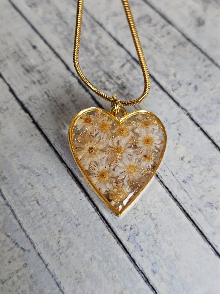 Close up of cream mini flowers in a gold tone heart shaped pendant on a wooden background.