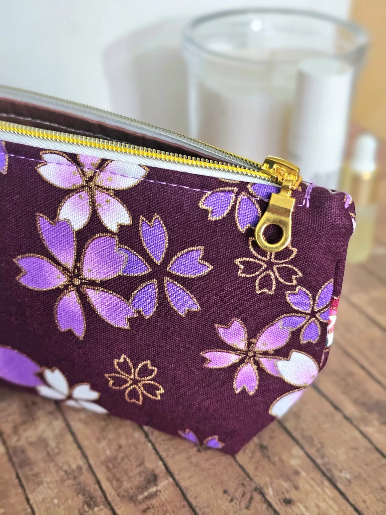 Close up of a corner of gold foiled flowers on deep purple Toiletries bag with gold zip.