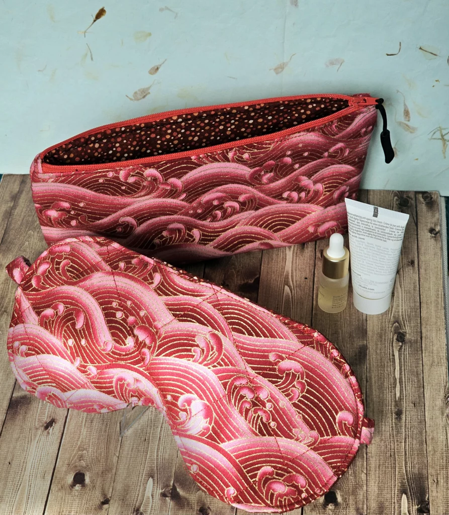 Matching sleep mask and toiletries bag made with red gold foiled wave fabric styled with mini toiletries.