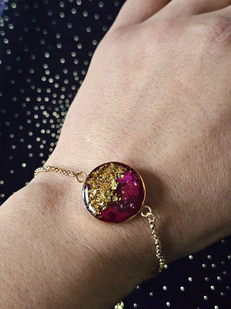 Lady's wrist wearing a gold tone stainless steel bezel bracelet made with gold flakes and red rose petal.